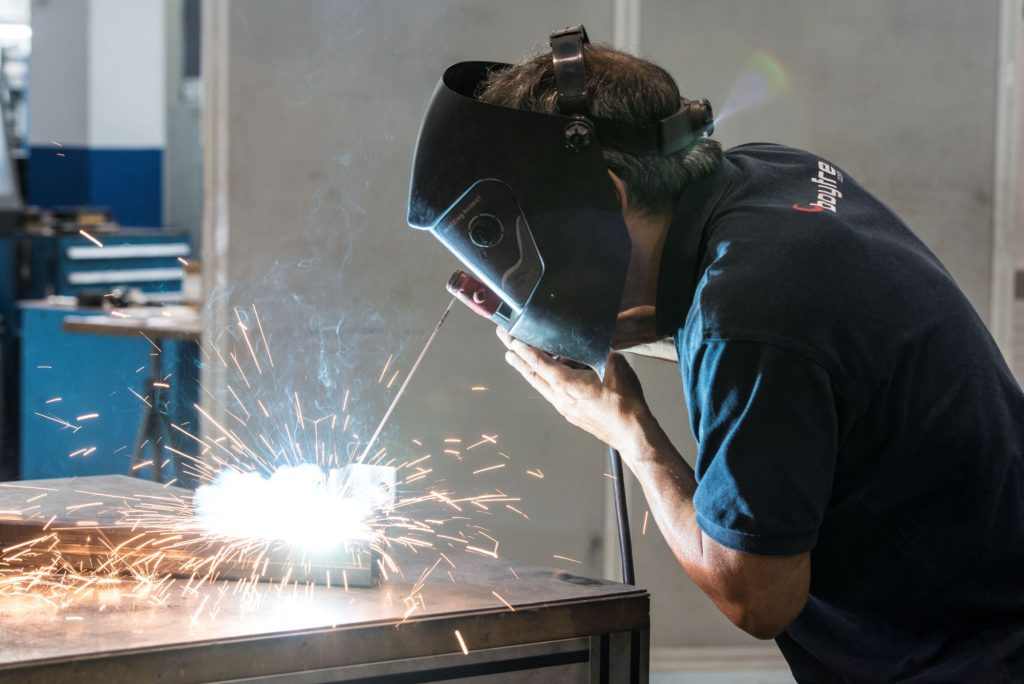 Un hombre realizando una soldadura con el casco protector puesto frente a las chispas que salen del trabajo.